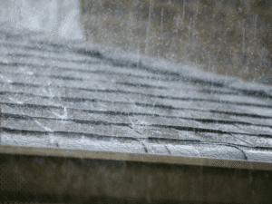 Close-up of rain impacting asphalt roof shingles, demonstrating importance of roof inspection in Lafayette LA