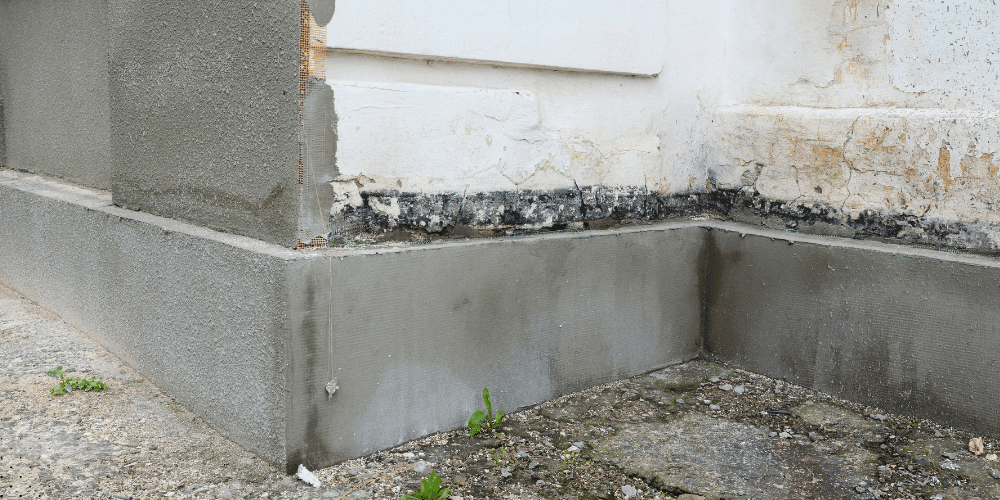 Foundation corner with recent patching and moisture damage at base of exterior wall