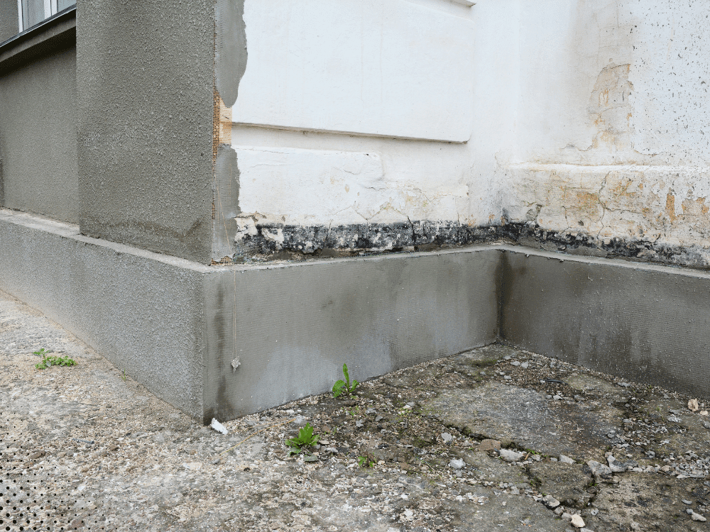 Foundation corner with recent patching and moisture damage at base of exterior wall